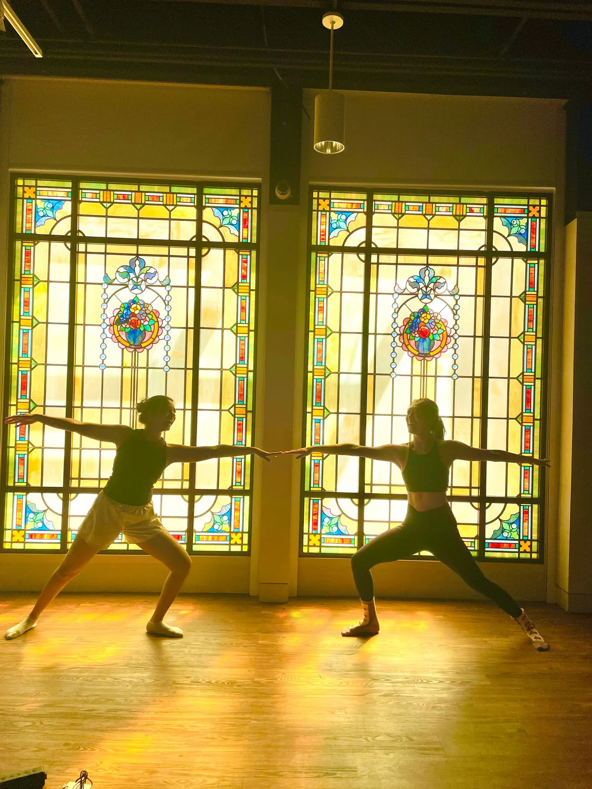 Two people in a yoga pose against stained-glass windows in warm light