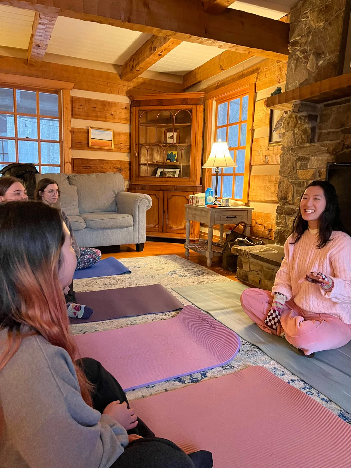 Ashley, in pink, leading a small yoga class in a wood-beamed cabin